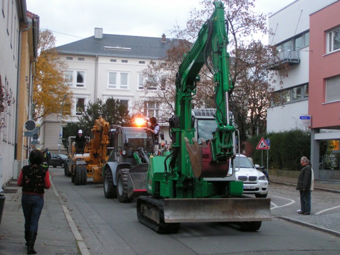 Eine Kolonne von Baggern fahren durch die Sedanstraße Richtung Museum, auf beiden Straßenseiten sehen Passanten zu