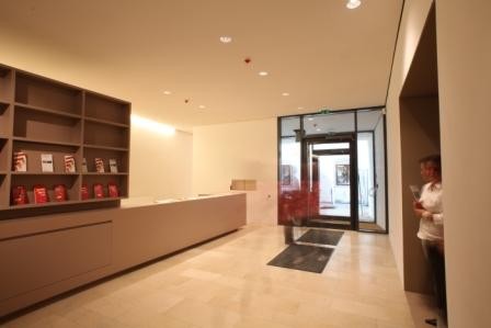 Blick ins Museumsfoyer, im Hintergrund die Eingangstür, links der Museumsshop mit teilweise gefüllten Regalen, rechts eine Besucherin in der Türe zur Dauerausstellung