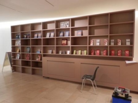 Blick auf die teilweise gefüllten Regale des Museumsshops, im Vordergrund ein Stuhl und ein Werkzeugkasten