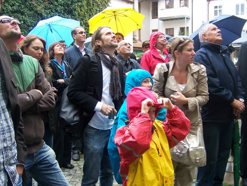 eine Gruppe von Personen im Kaisergäßchen schauen nach oben, teilweise mit Regenschirm und Regenkleidung