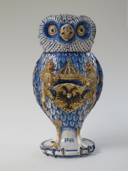 Pokal in Form einer stehenden Eule, blau bemalt und auf der Brust das Wappen mit einem zweiköpfigen Adler, links und rechts davon halten zwei Löwen eine Krone über das Wappen.