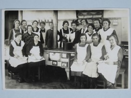 altes Foto: Hauswirtschaftskurs an der Kochmaschine. 17 Frauen stehen um einen alten Herd versammelt und schauen in die Kamera.