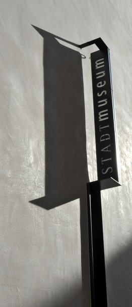 Metallschild des Stadtmuseums an der Außenfassade mit senkrechter Aufschrift STADTmuseum