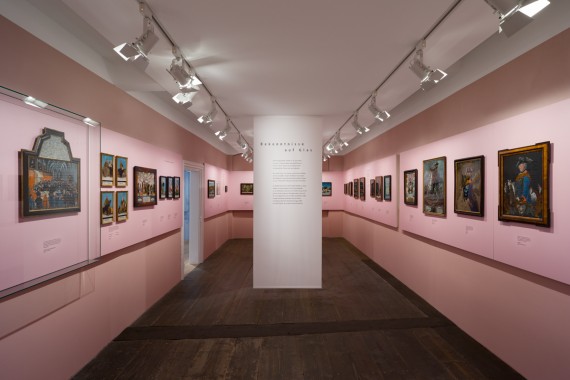 Blick in den Ausstellungsraum der Hinterglasbilder, an den rosa gestrichenen Wänden hängen, teilweise in Gruppen, Hinterglasbilder