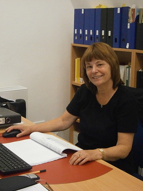 Frau Gräser am Computer sitzend, vor ihr auf dem Schreibtisch liegen Unterlagen
