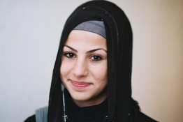 Portrait von Gamze E.. sie trägt ein schwarzes Kopftuch und lächelt in die Kamera.