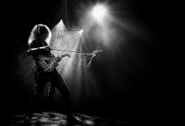 Schwarz-weiß Foto mit einem E-Gitarrenspieler mit Geigenbogen im Hintergrund Lichteffekte