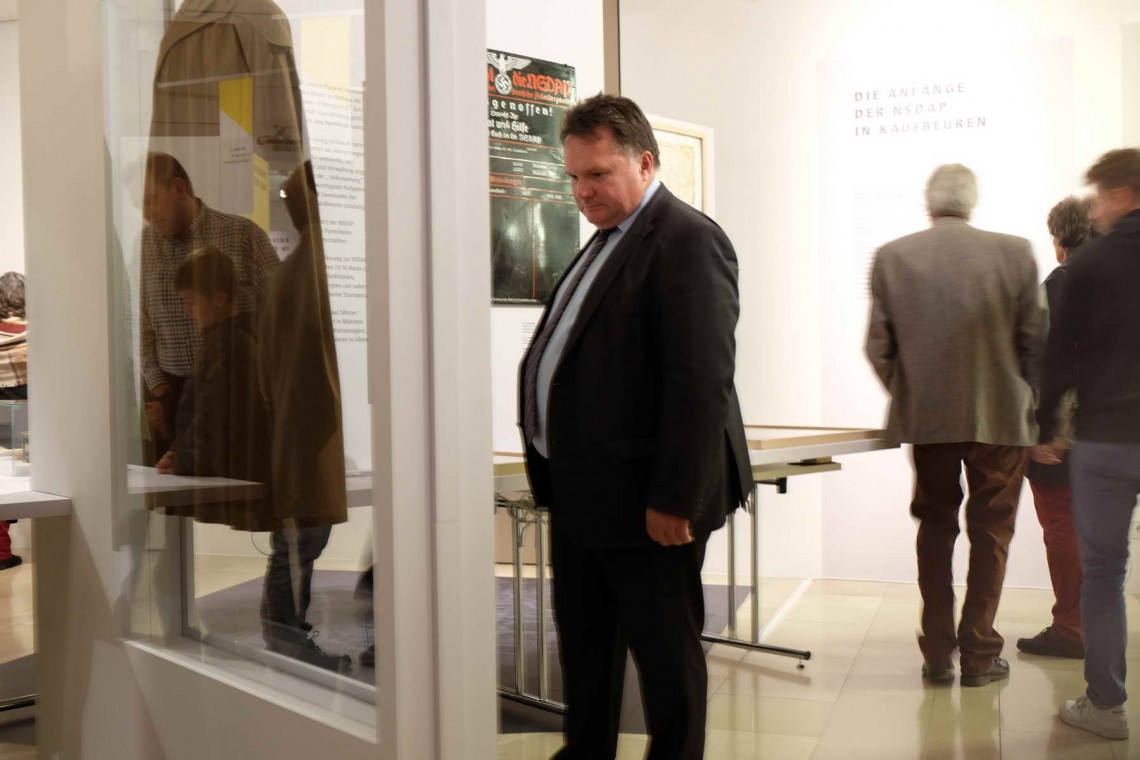 Stefan Bosse begutachtet einen BDM-Mantel. Im Hintergrund mehrere Menschen, die sich ebenfalls die Ausstellung ansehen.