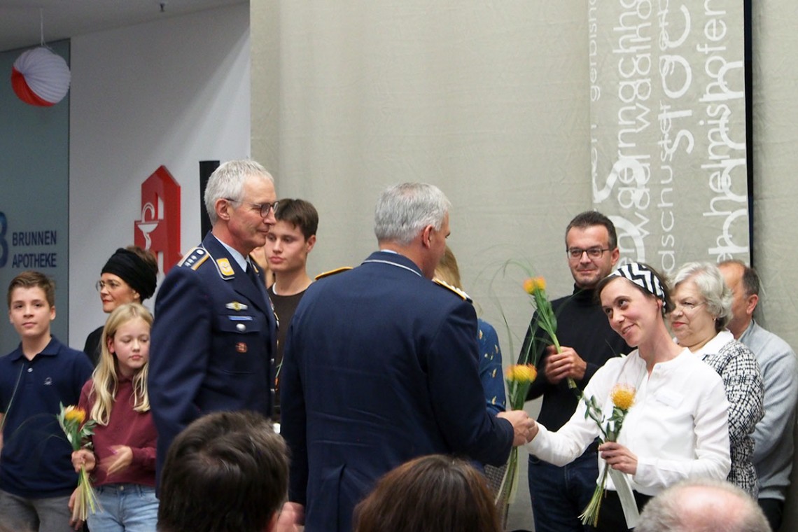 Museumsleiterin Petra Weber verteilt Blumen an zwei uniformierte Vertreter der Bundeswehr. Im Hintergrund stehen mehrere Kinder und Erwachsene, die bereits eine Blume bekommen haben.
