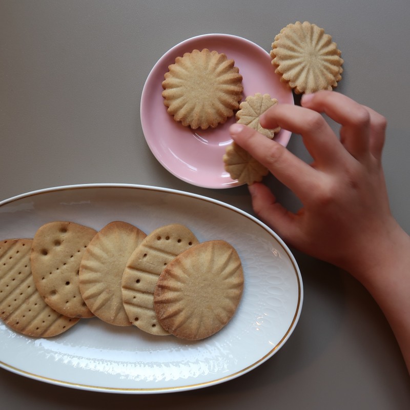Ein großer und ein kleiner Teller, darauf selbst gebackene Kekse, eine Hand nimmt einen Keks