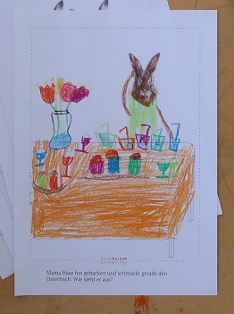 Kinderzeichnung eines Hasen vor einem Tisch mit Blumenvase und bunten Gläsern