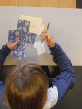 Kind schneidet die blau gemusterte Schachtelvorlage aus