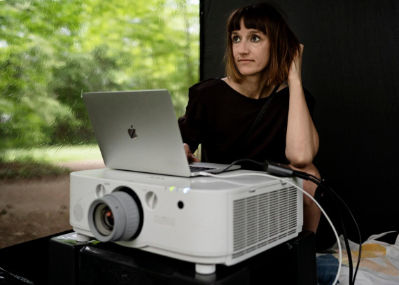Videokünstlerin Vanessa Hafenbrädl sitzend hinter einem Beamer mit einem Laptop darauf