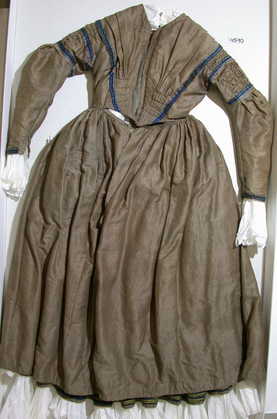 Frauenkleid, zweite Hälfte 19. Jahrhundert. Ein braunes Kleid, mit einer Borte am Hals, an den Ärmeln und am Saum.
