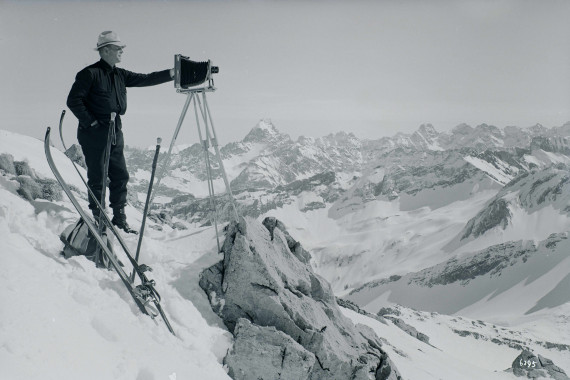 Mann mit Skiern und Plattenkamera auf verschneiten Bergen.