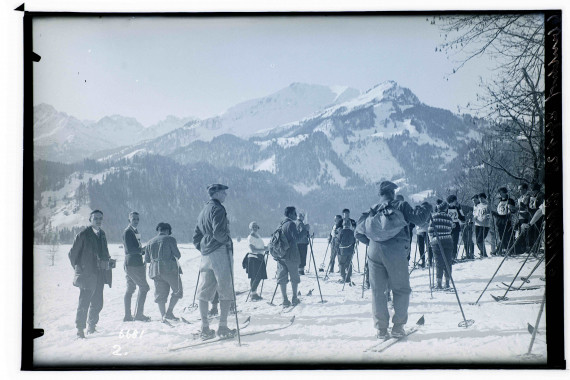 Viele Skifahrer im flachen Gelände, verschneite Berge im Hintergrund.